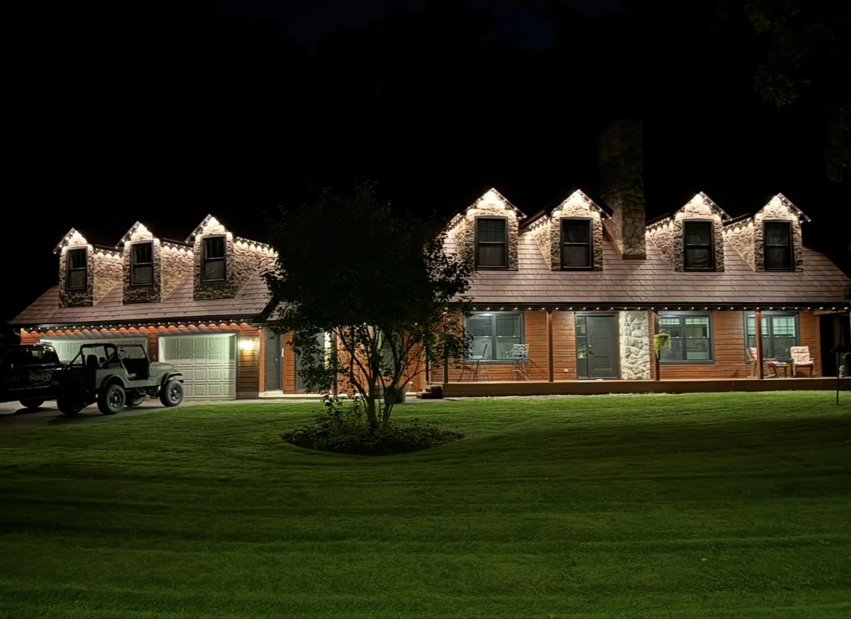 Burlington home illuminated at night with warm white permanent Christmas lighting installed along the roofline and dormers.