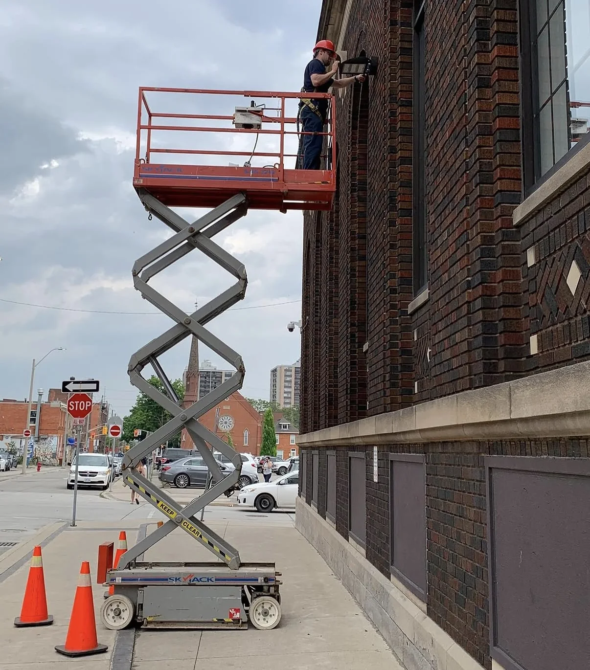 Electrician on a scissor lift installing an outdoor light on a historic brick building.