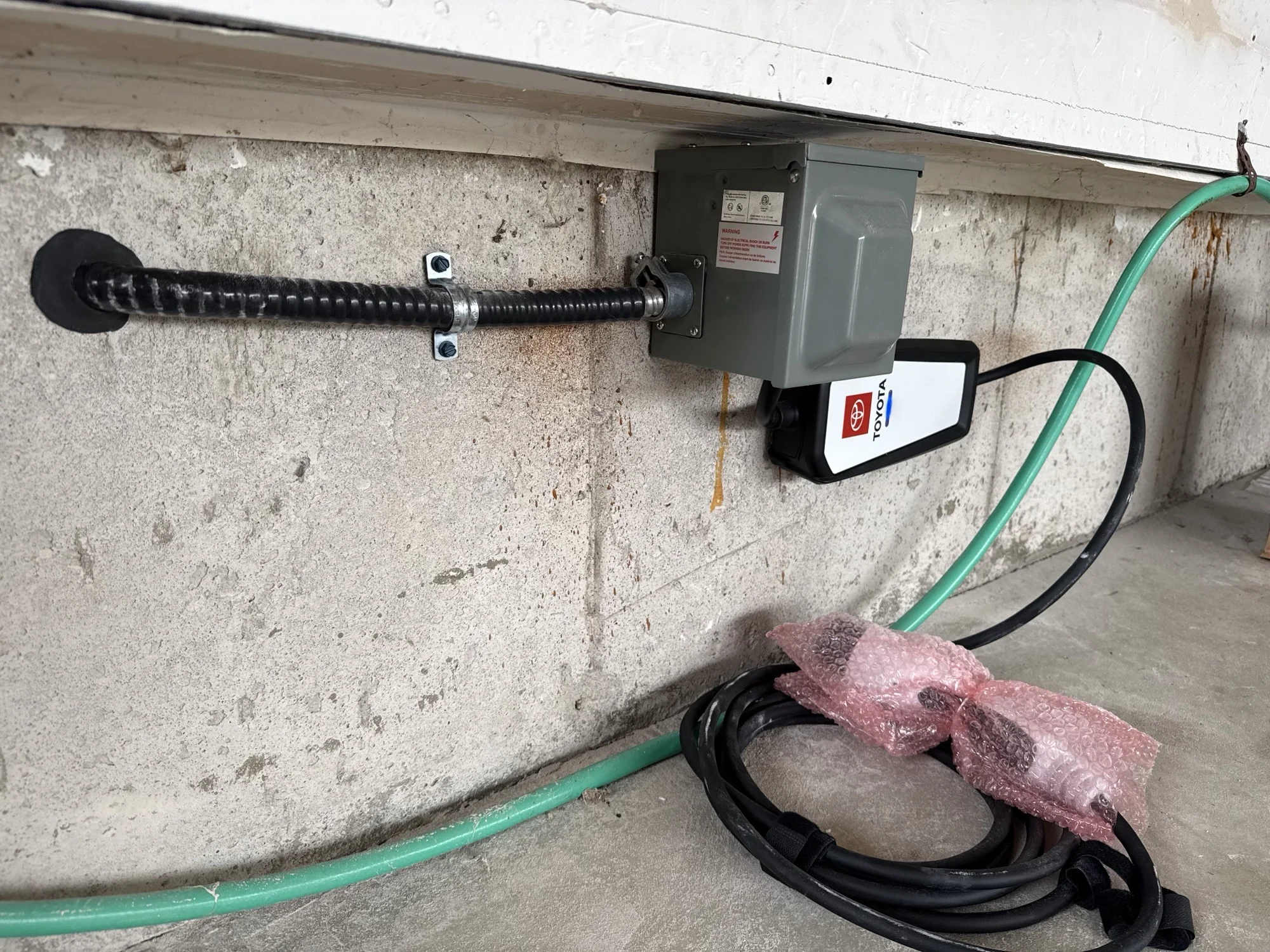 A 50 amp residential EV charging connection mounted on a concrete garage wall in Oakville, with a Toyota portable charging cable connected.