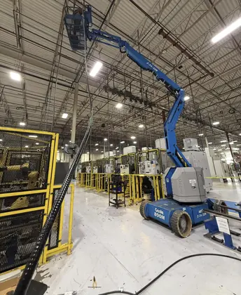 Blue Genie boom lift beside industrial equipment during a robot charger electrical installation.