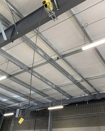Yellow retractable cord reel mounted to a steel ceiling beam above a work area.