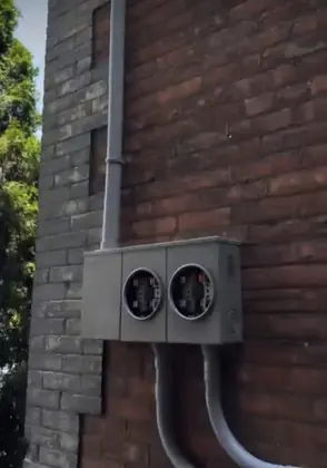 Two outdoor electricity meter positions mounted on a brick wall with connected conduit.